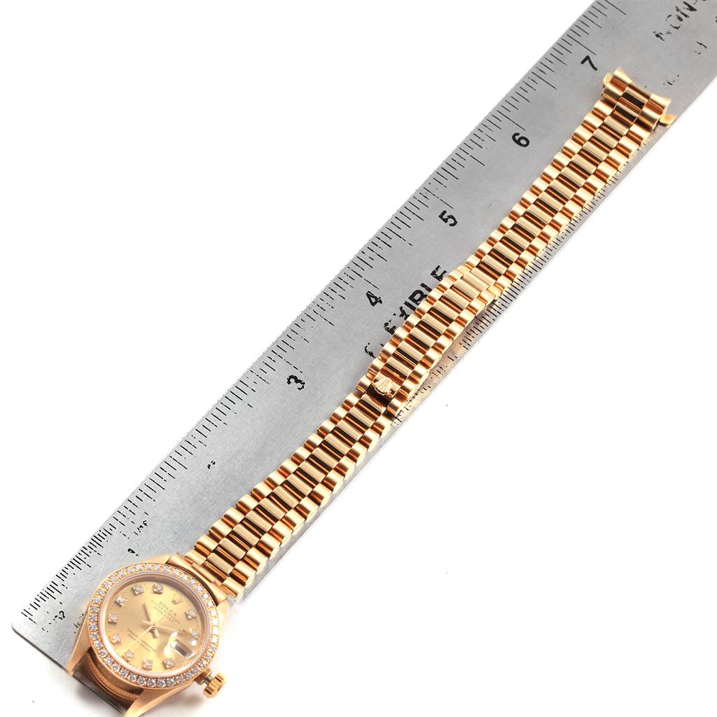 The image shows a Rolex President 69138 Women's Yellow Gold Champagne Dial 69138 Women's Yellow Gold Champagne Dial model watch placed adjacent to a ruler, displaying its full band and dial from a top-down angle.