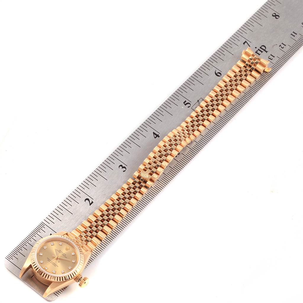 The image shows a top-down view of a Rolex President 67198 Women
s Yellow Gold Champagne Dial 67198 Women
s Yellow Gold Champagne Dial model watch with its band alongside a ruler for measurement.