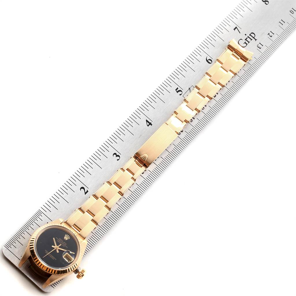 The image shows a Rolex President 6917 Women
s Yellow Gold Black Dial 6917 Women
s Yellow Gold Black Dial model watch laid flat next to a ruler, highlighting the bracelet and face.