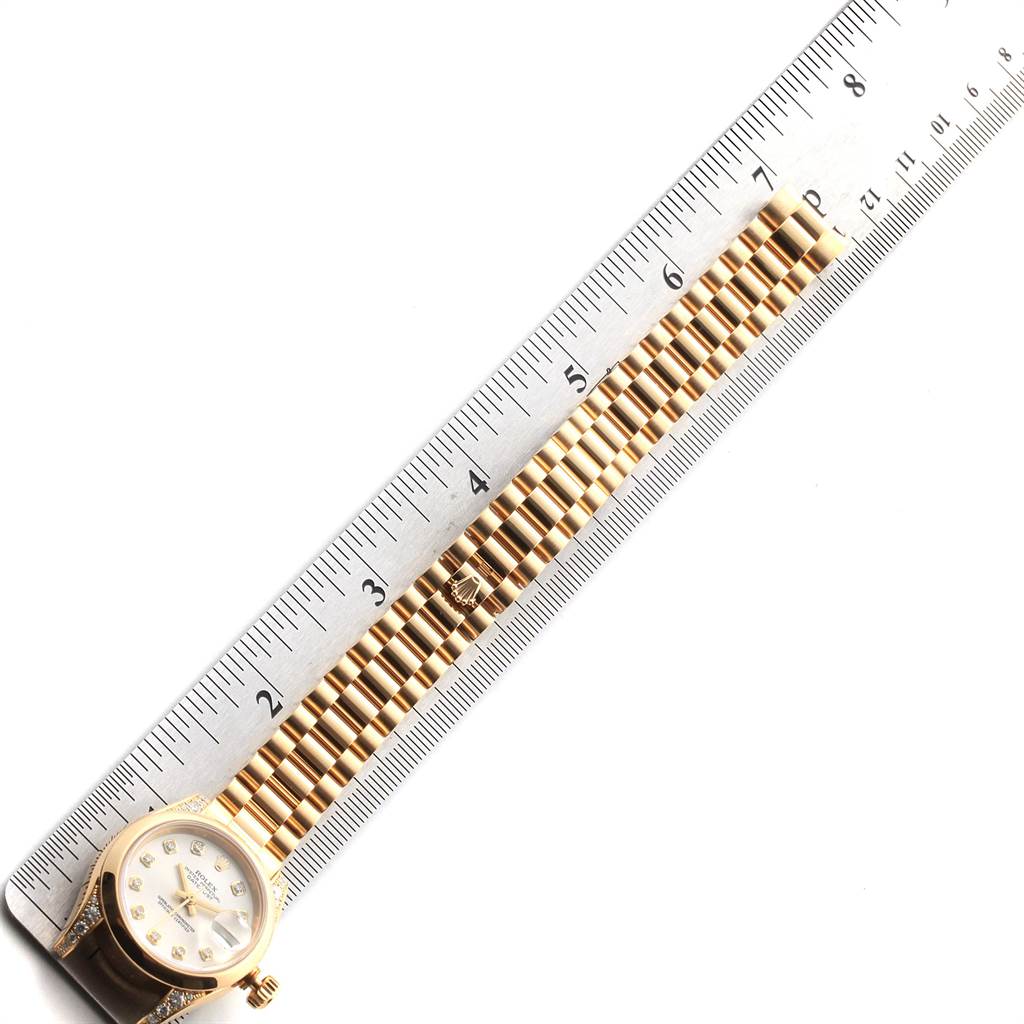 The image shows a Rolex President 179298 Women's Yellow Gold Silver Dial 179298 Women's Yellow Gold Silver Dial model watch laid next to a ruler, displaying the face and band.