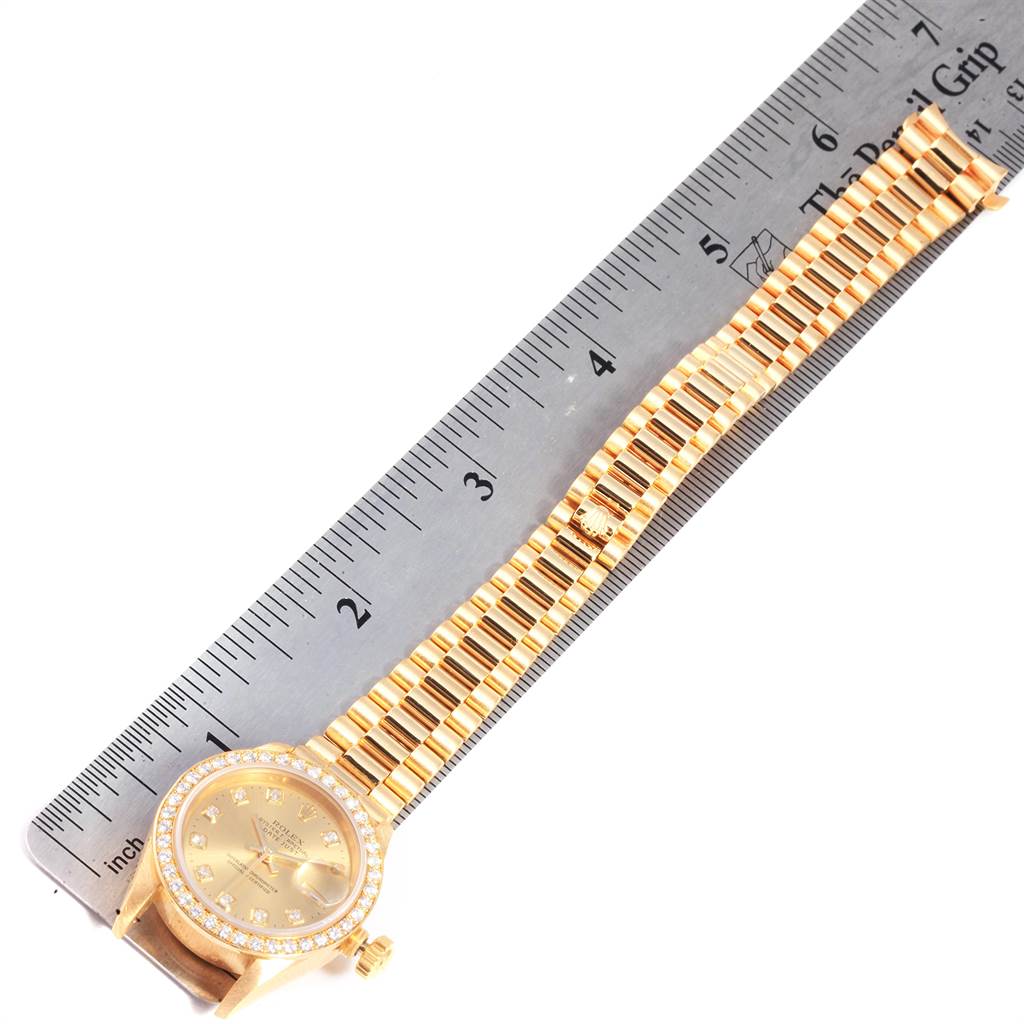 The image shows a Rolex President 69138 Women
s Yellow Gold Champagne Dial 69138 Women
s Yellow Gold Champagne Dial model watch laid flat next to a ruler, displaying the watch face and band in full.