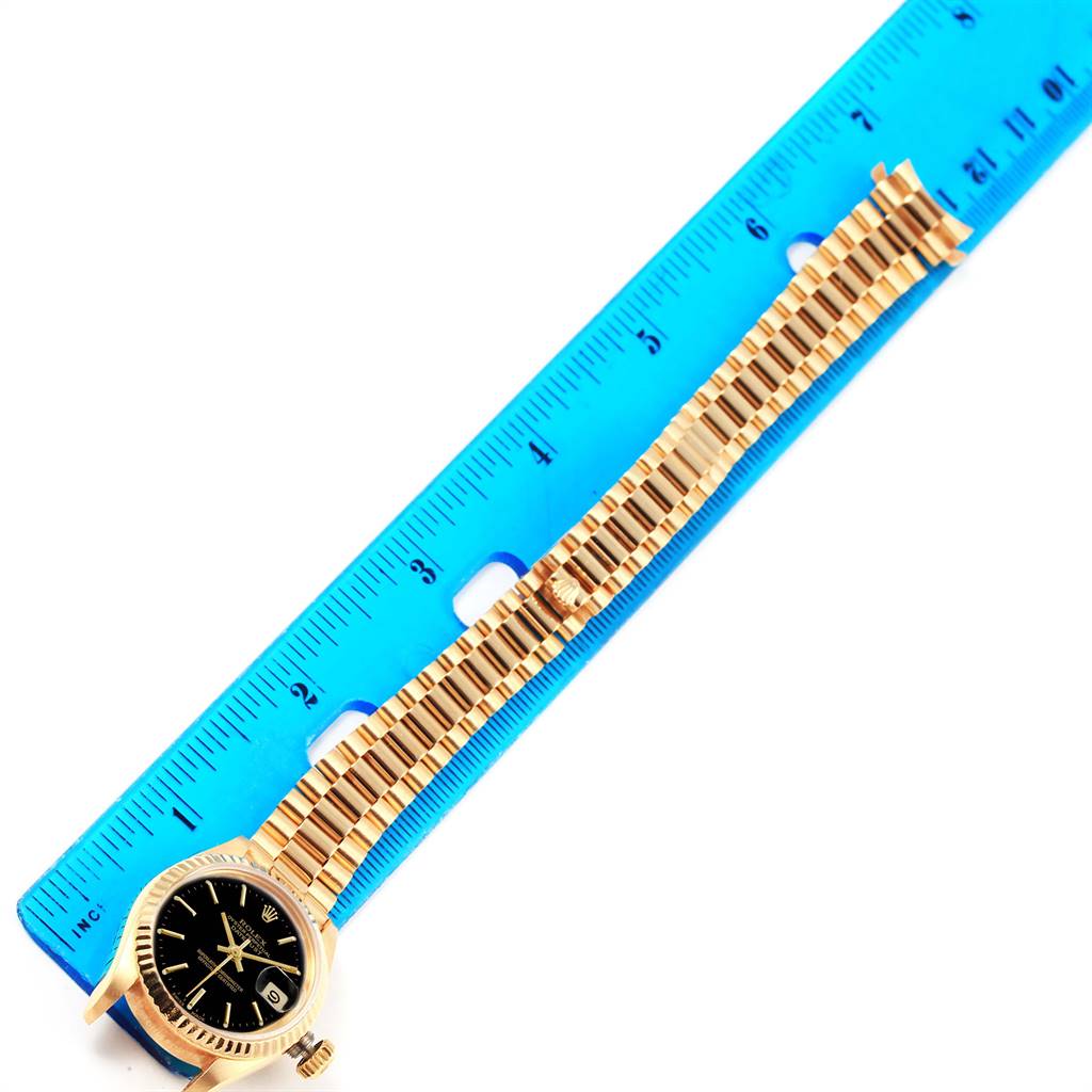 The image shows a Rolex President 69178 Women's Yellow Gold Black Dial 69178 Women's Yellow Gold Black Dial model watch lying flat along a blue ruler, displaying its face, bezel, and gold bracelet.