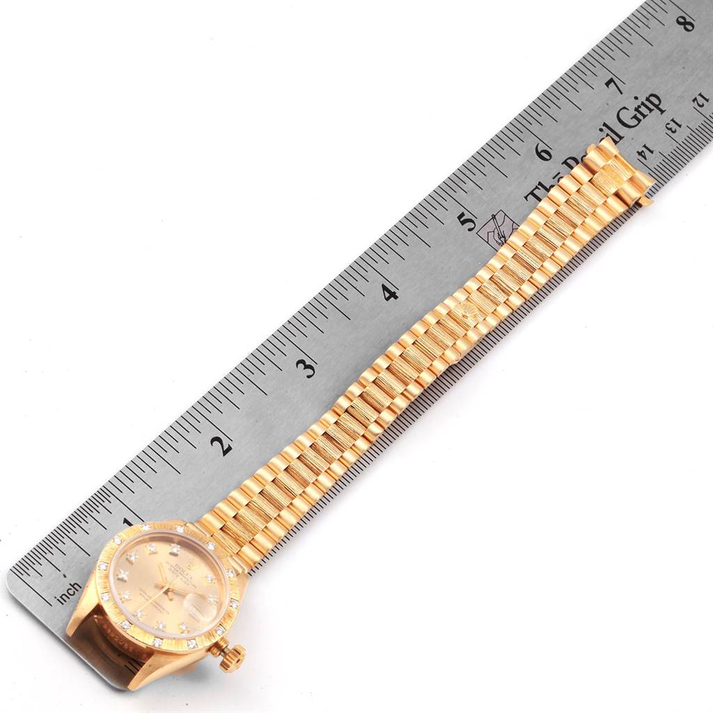 The image displays a Rolex President 69288 Women
s Yellow Gold Champagne Dial 69288 Women
s Yellow Gold Champagne Dial model watch laid flat next to a ruler, showing the watch face and bracelet.
