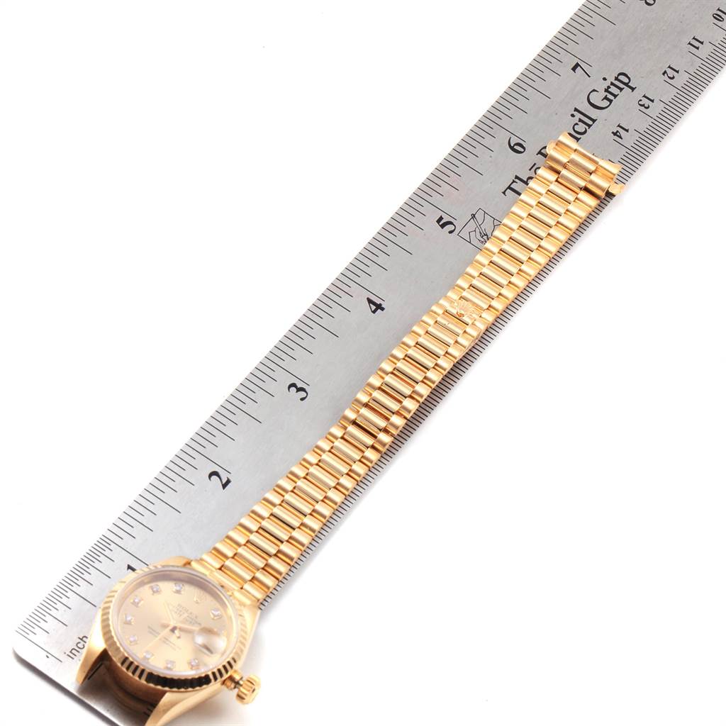 This image shows a Rolex President 69178 Women
s Yellow Gold Champagne Dial 69178 Women
s Yellow Gold Champagne Dial model watch laid flat alongside a ruler, displaying the watch face and bracelet.