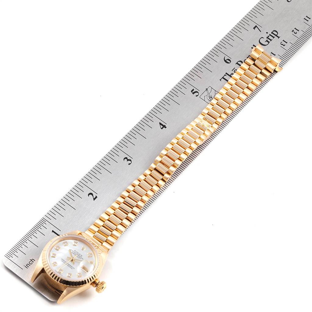 The image shows a Rolex President 79178 Women
s Yellow Gold Mother of Pearl Dial 79178 Women
s Yellow Gold Mother of Pearl Dial watch laying flat with its band and face measured against a ruler.