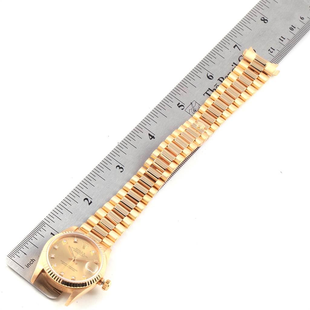 The image shows a Rolex President 68278 Women
s Yellow Gold Champagne Dial 68278 Women
s Yellow Gold Champagne Dial model watch laid flat beside a ruler, displaying its bracelet and the watch face.