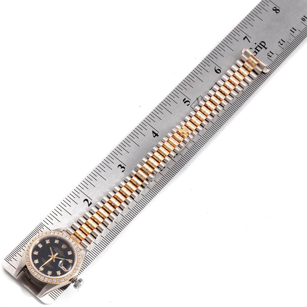 The image shows a Rolex President 69179 Women's White Gold Black Dial 69179 Women's White Gold Black Dial model watch laid flat next to a ruler, highlighting its face and two-toned bracelet.