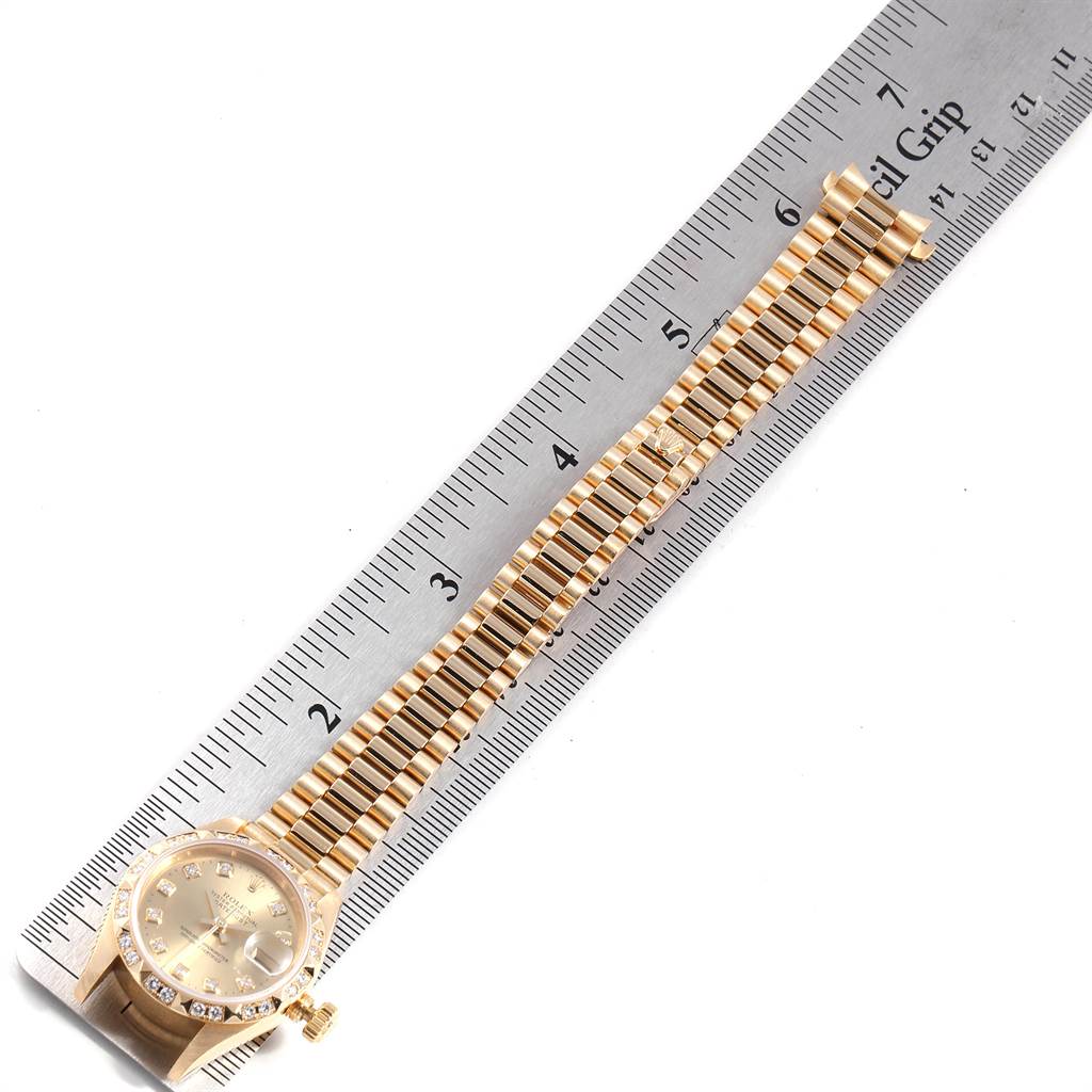 The image shows a Rolex President 69258 Women
s Yellow Gold Champagne Dial 69258 Women
s Yellow Gold Champagne Dial watch laid next to a ruler, displaying its watch face and bracelet.