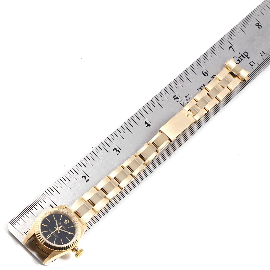 This image shows a Rolex President 67198 Women's Yellow Gold Black Dial 67198 Women's Yellow Gold Black Dial model watch laid flat next to a ruler, displaying its entire band and watch face from a top-down angle.