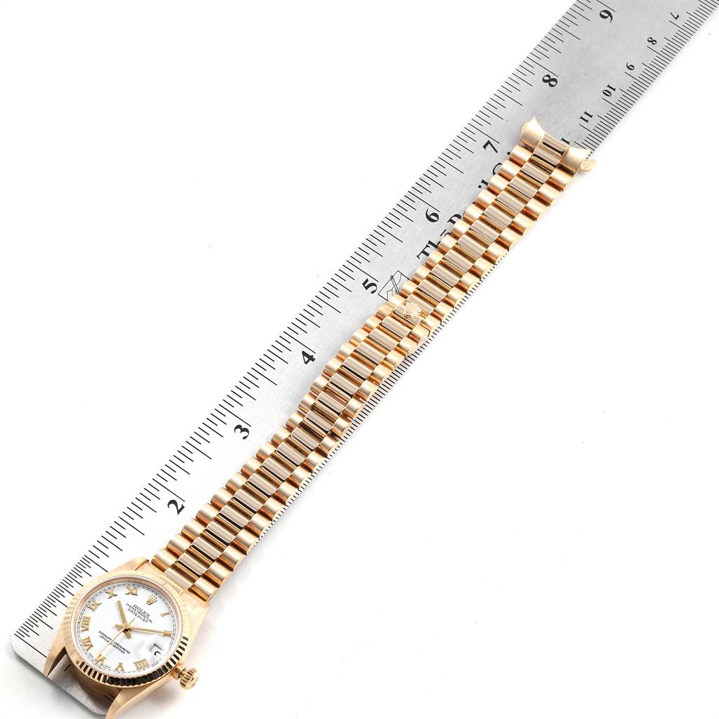 The image shows a President model Rolex watch placed alongside a ruler, showcasing its bracelet and face from a top-down angle.
