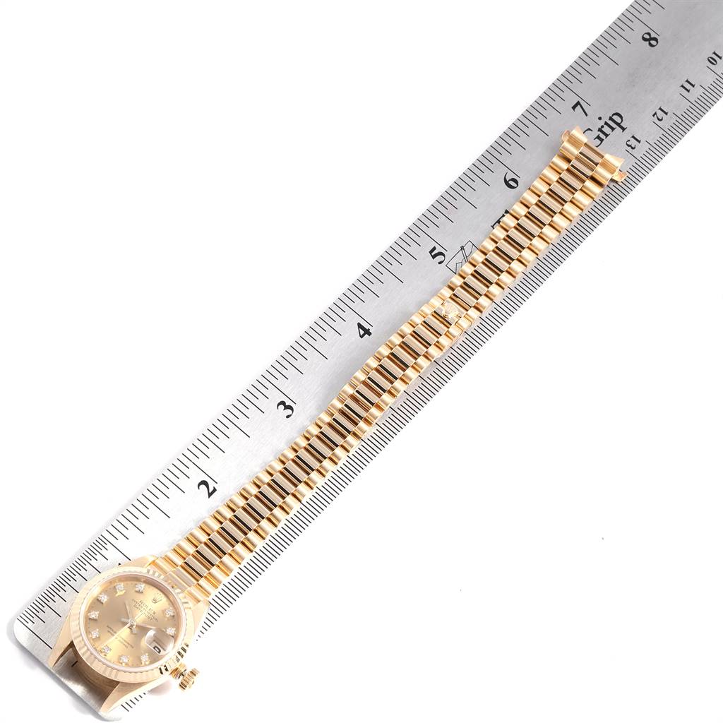 The image shows a Rolex President 69178 Women's Yellow Gold Champagne Dial 69178 Women's Yellow Gold Champagne Dial model watch with a ruler measuring its bracelet laid out flat.