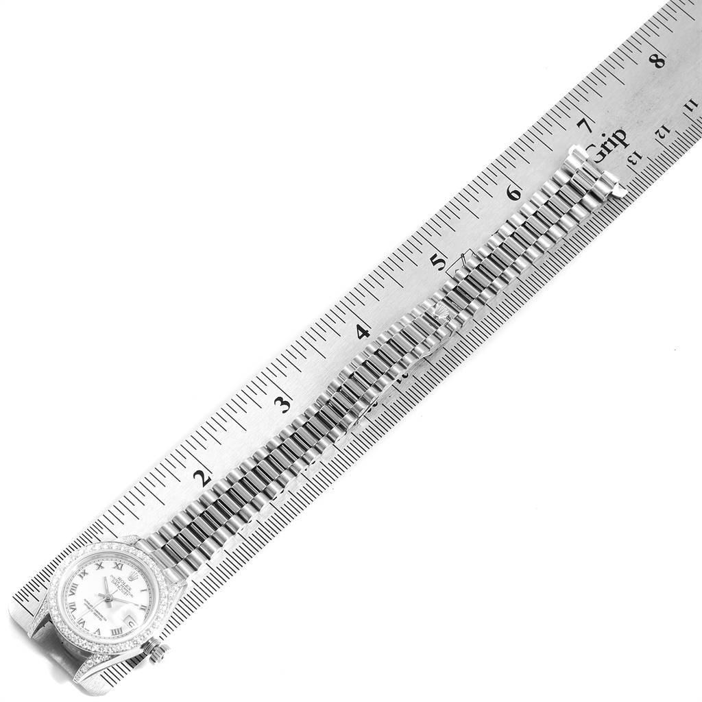 The image shows a Rolex President 69159 Women's White Gold White Dial 69159 Women's White Gold White Dial model watch laid flat next to a ruler, showcasing its band and face.