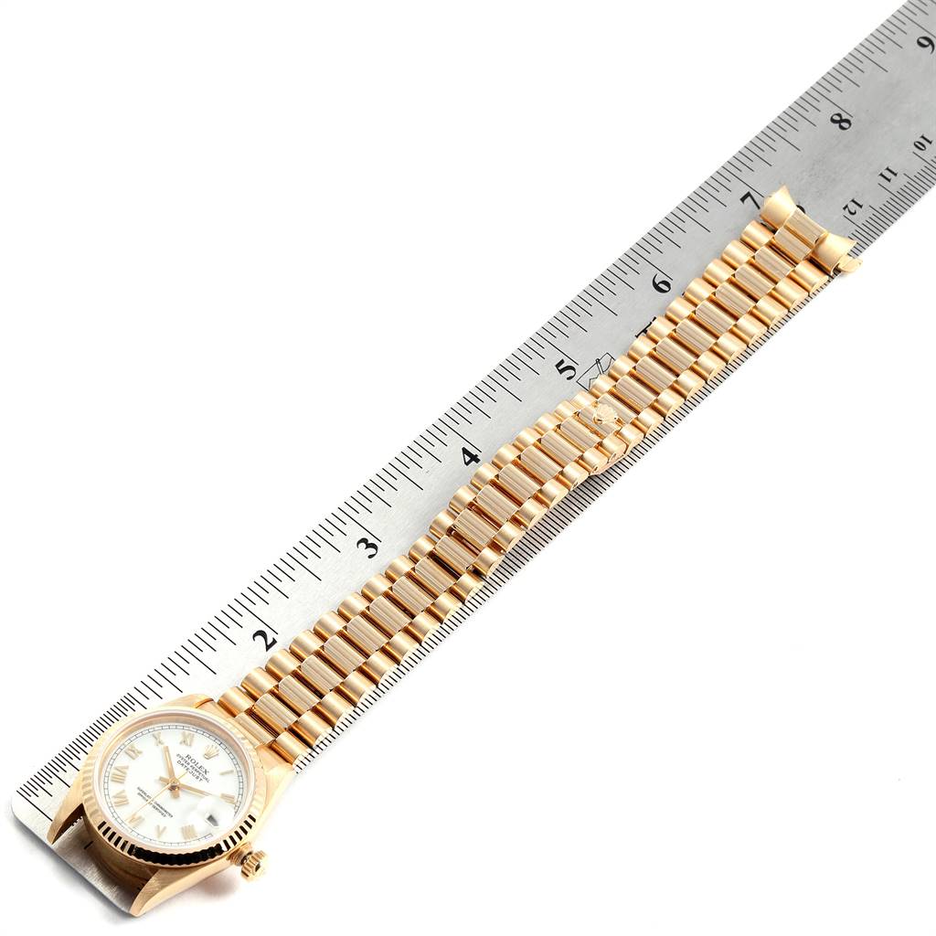 The image shows a gold Rolex President 68278 Women's Yellow Gold White Dial 68278 Women's Yellow Gold White Dial model watch laid flat against a ruler, highlighting its bracelet and face.