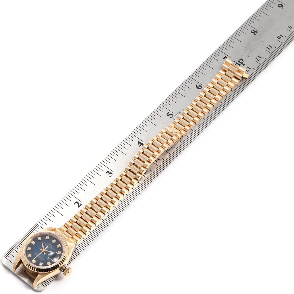 The image shows a Rolex President 69178 Women's Yellow Gold Blue Dial 69178 Women's Yellow Gold Blue Dial model watch laid flat on a ruler, displaying its face and band.