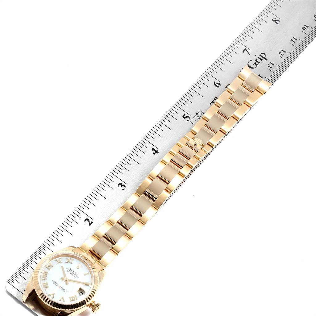 The image shows an overhead view of a Rolex President 178278 Women
s Yellow Gold Mother of Pearl Dial 178278 Women
s Yellow Gold Mother of Pearl Dial model watch, including its face and bracelet, next to a ruler for scale.