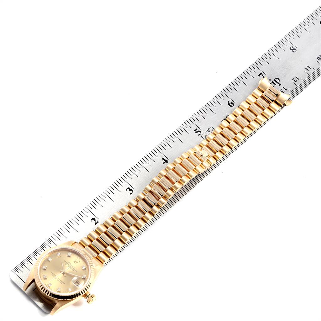The image shows a Rolex President 68278 Women
s Yellow Gold Champagne Dial 68278 Women
s Yellow Gold Champagne Dial model watch laid flat against a ruler, displaying the dial, bezel, and band.