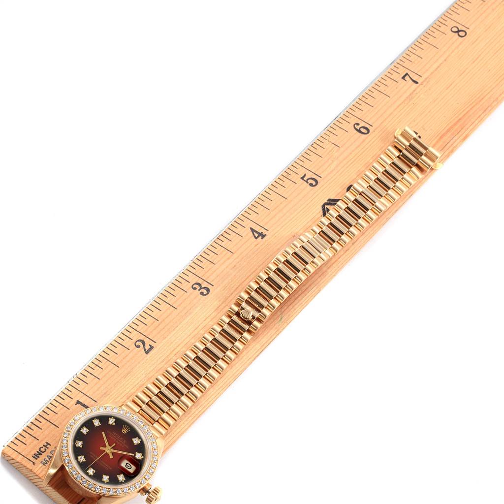 The Rolex President 69138 Yellow Gold Red Dial 69138 Yellow Gold Red Dial model watch is shown in a top-down view, featuring its face, bezel, and bracelet alongside a ruler.