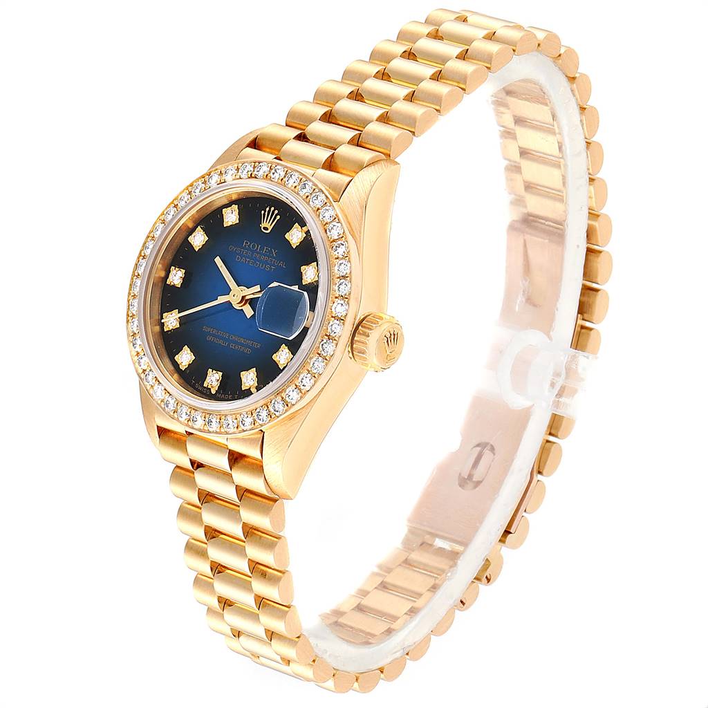 The watch is a Rolex President 69138 Women's Yellow Gold Blue Dial 69138 Women's Yellow Gold Blue Dial model shown at an angle highlighting its gold bracelet, blue dial, and diamond-encrusted bezel.