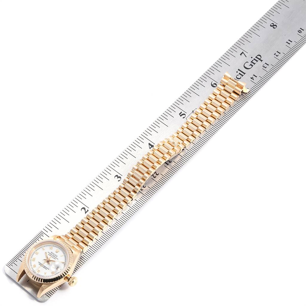 The image shows a President model Rolex watch laid flat along a metal ruler, displaying the face and entire bracelet.