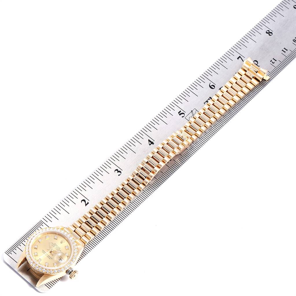 This image shows a Rolex President 69138 Women
s Yellow Gold Champagne Dial 69138 Women
s Yellow Gold Champagne Dial model watch placed alongside a ruler, displaying its bracelet and watch face.