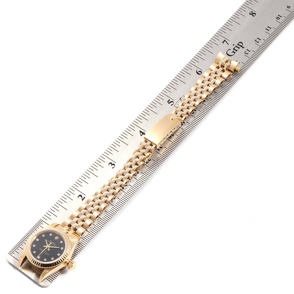 The image shows a horizontal view of a Rolex President 67198 Women's Yellow Gold Black Dial 67198 Women's Yellow Gold Black Dial model watch with the face, band, and clasp extended along a ruler.