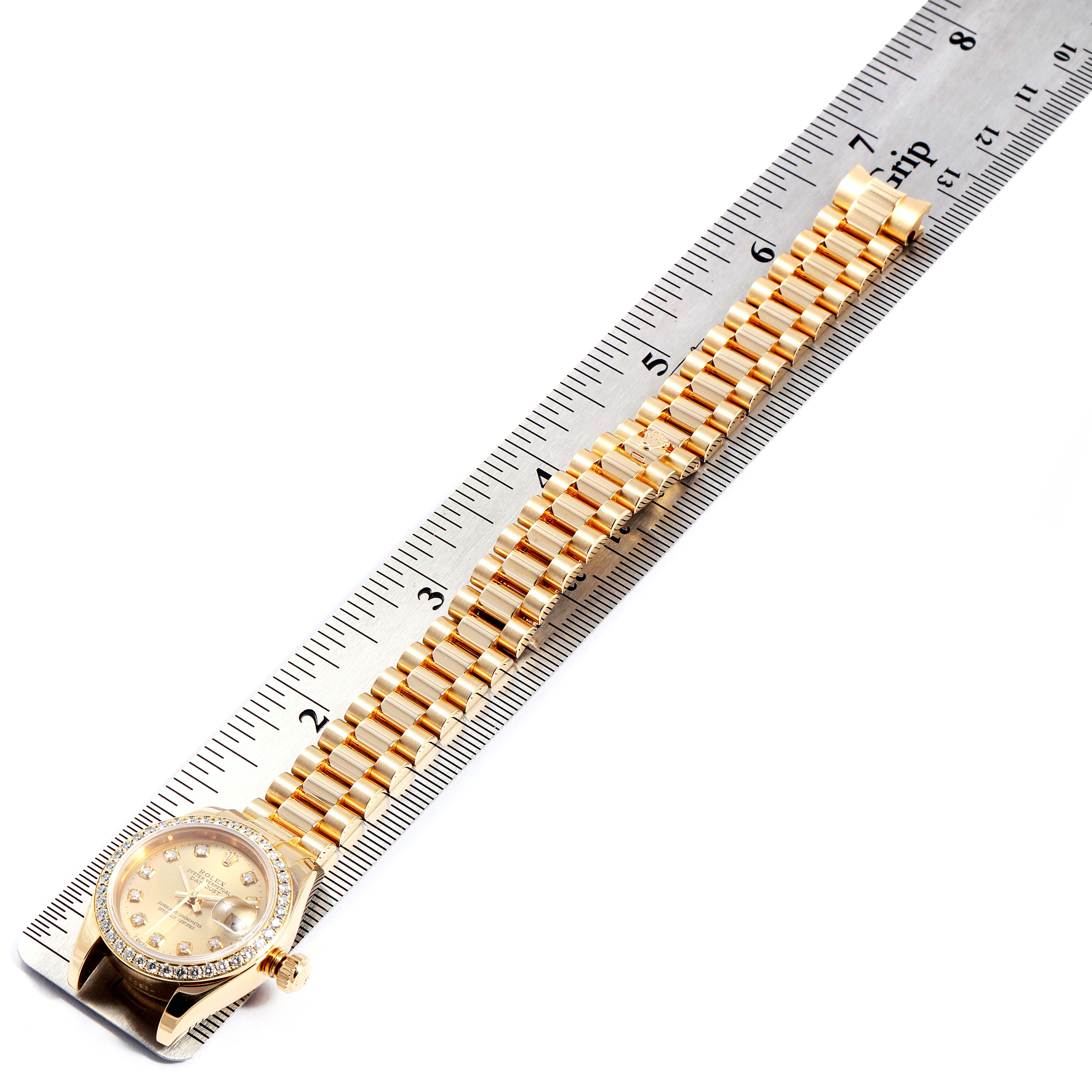 This image shows the face and bracelet of a Rolex President 179178 Women
s Yellow Gold Champagne Dial 179178 Women
s Yellow Gold Champagne Dial model watch positioned on a ruler, displaying a side view angle.