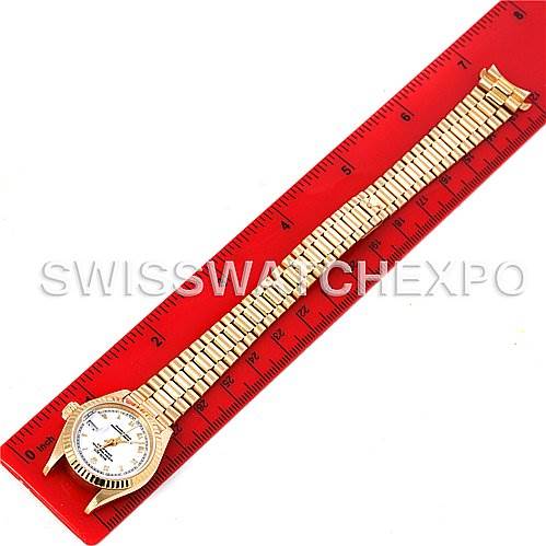 The image shows a Rolex President 69178 Women's Yellow Gold White Dial 69178 Women's Yellow Gold White Dial model watch placed next to a red ruler, displaying the entire watch band and face from a top-down angle.