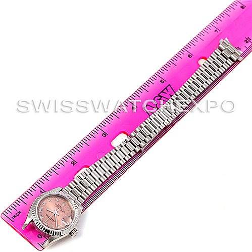 The Rolex President 79179 Women's White Gold Pink Dial 79179 Women's White Gold Pink Dial model watch is shown from a top-down angle, highlighting the watch face, bezel, and bracelet aligned with a pink ruler.