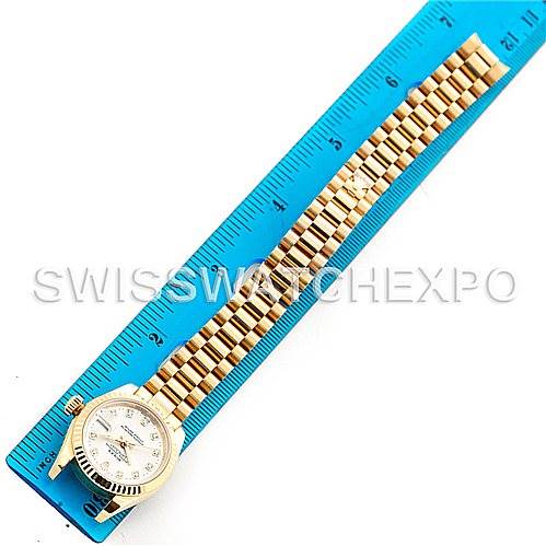 The image shows a top view of a Rolex President 179178 Women
s Yellow Gold Silver Dial 179178 Women
s Yellow Gold Silver Dial model watch with the band extended next to a blue ruler.