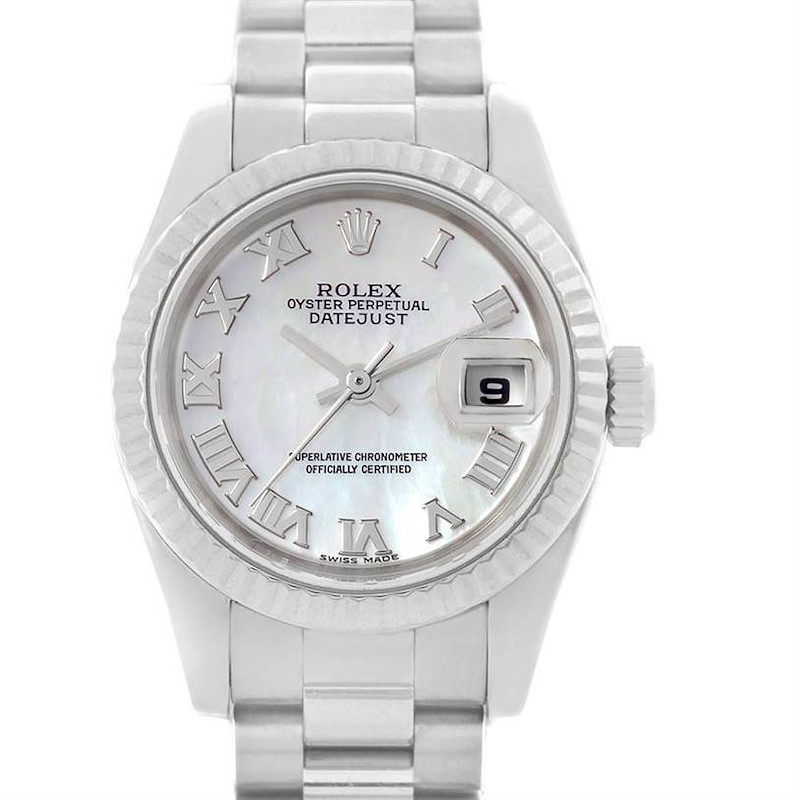 The image shows a Rolex President model watch with a white dial, Roman numerals, date window, and silver bracelet from a front angle.