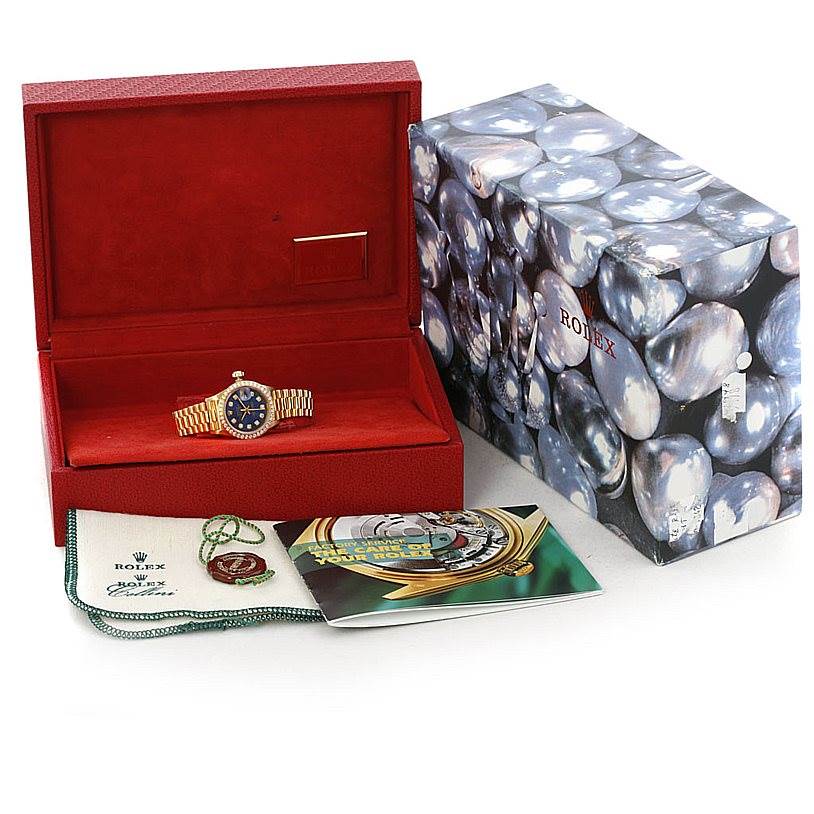 This image shows a Rolex President 69138 Women's Yellow Gold Blue Dial 69138 Women's Yellow Gold Blue Dial model watch inside an open red box, with a booklet and accessories placed in front.