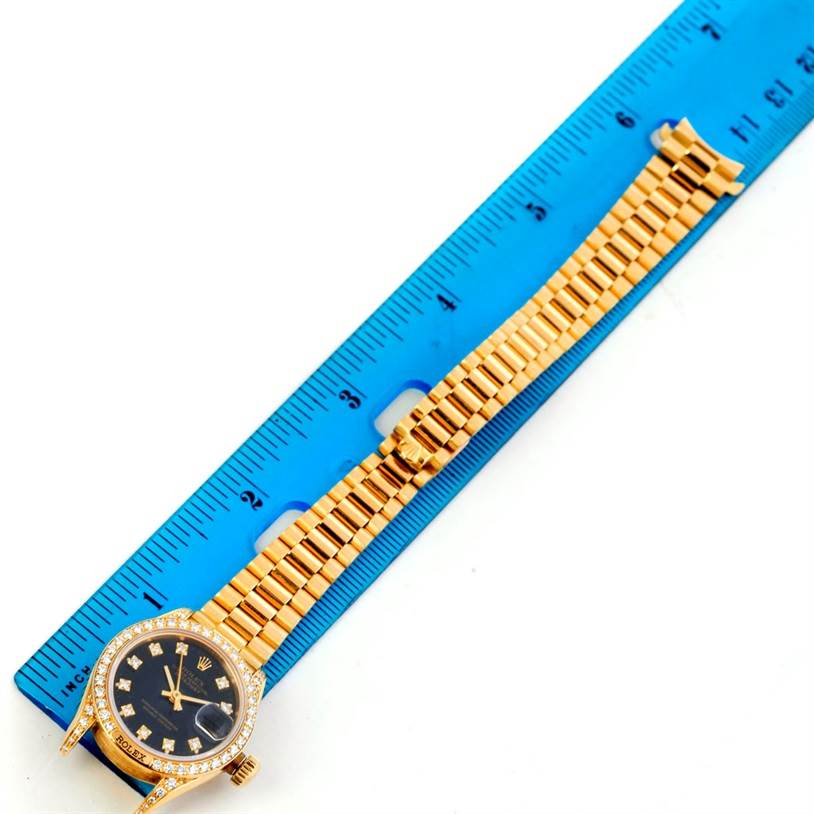 The Rolex President 69158 Women's Yellow Gold Black Dial 69158 Women's Yellow Gold Black Dial model watch is shown lying flat with the dial, bezel, and full bracelet visible next to a blue ruler.