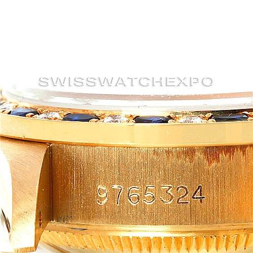 The image shows a close-up of the side of a Rolex President 69198 Women's Yellow Gold Blue Dial 69198 Women's Yellow Gold Blue Dial watch, highlighting its serial number and part of the bezel with gemstones.
