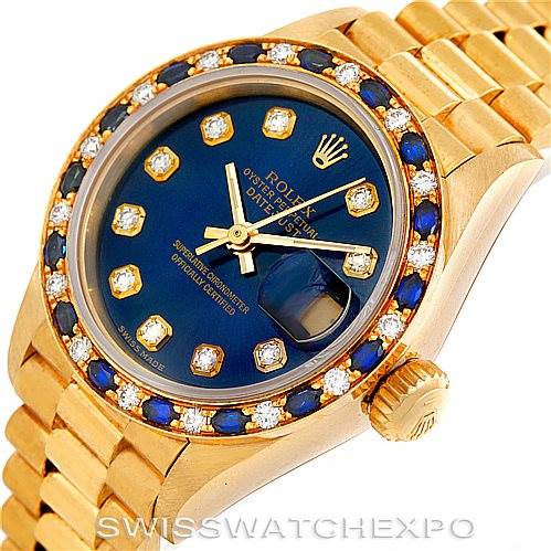 The image shows a Rolex President 69198 Women's Yellow Gold Blue Dial 69198 Women's Yellow Gold Blue Dial watch with a gold bracelet, blue dial, and gemstone-set bezel from an angled top view.