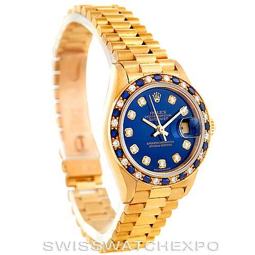 This image shows a Rolex President 69198 Women's Yellow Gold Blue Dial 69198 Women's Yellow Gold Blue Dial model watch at a three-quarter angle, highlighting its gold band, blue dial, and bejeweled bezel.