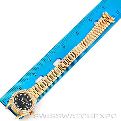 This image shows a Rolex President 69178 Women's Yellow Gold Black Dial 69178 Women's Yellow Gold Black Dial model watch placed alongside a blue ruler, showcasing its bracelet and face from a top-down angle.