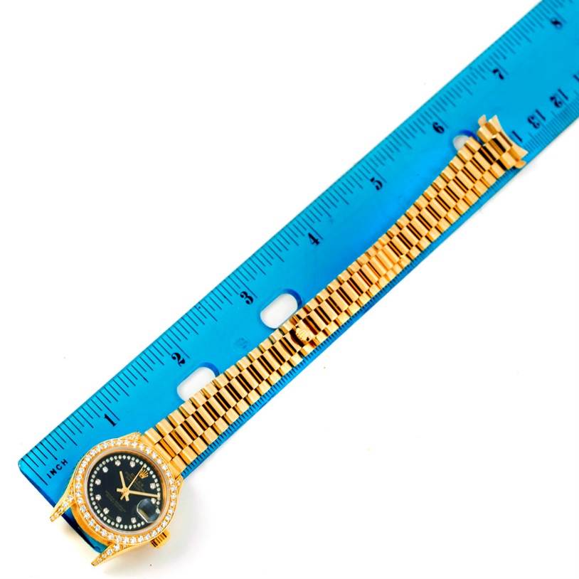 The Rolex President 69158 Women's Yellow Gold Black Dial 69158 Women's Yellow Gold Black Dial model watch is shown flat on a ruler, displaying its face and bracelet.