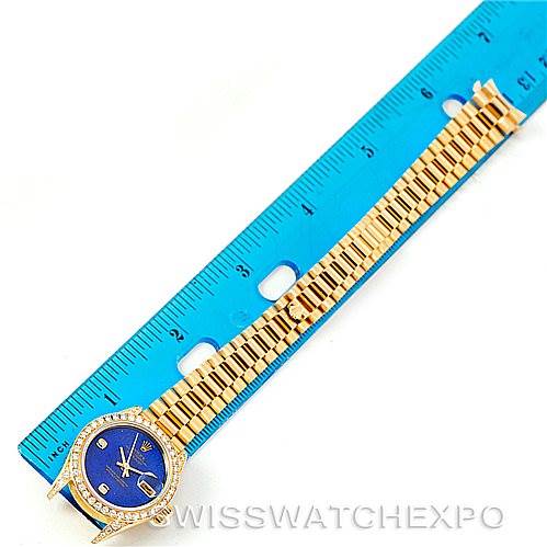 This image shows a Rolex President 79158 Women's Yellow Gold  79158 Women's Yellow Gold  model watch laid flat next to a blue ruler for size reference, highlighting its band and face.