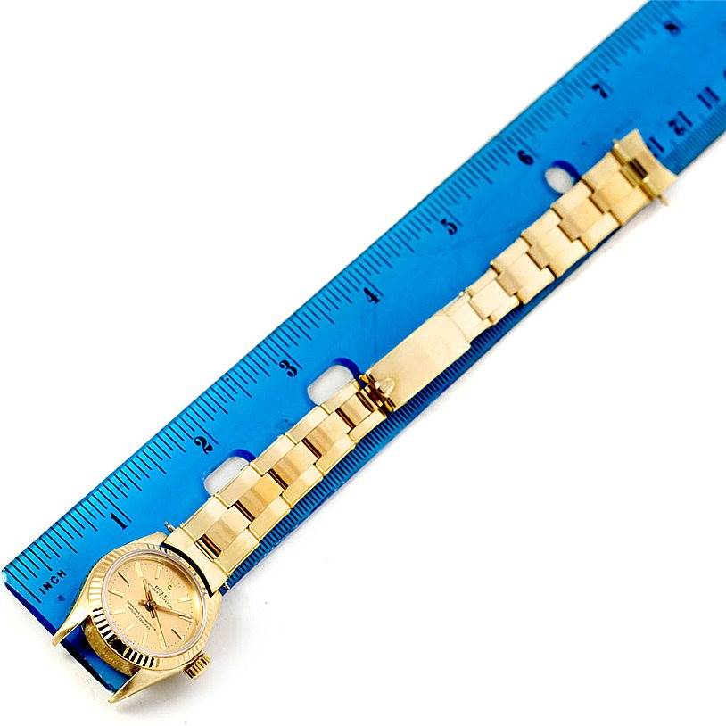 The image shows a Rolex President 67197 Women's Yellow Gold Champagne Dial 67197 Women's Yellow Gold Champagne Dial model watch laid flat next to a ruler, highlighting its gold bracelet and face.