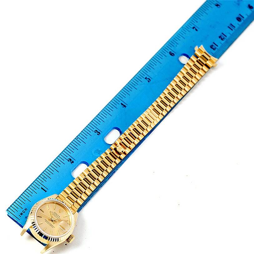 The image shows the face and bracelet of a Rolex President 69178 Women's Yellow Gold Champagne Dial 69178 Women's Yellow Gold Champagne Dial model, laying next to a blue ruler for size reference.