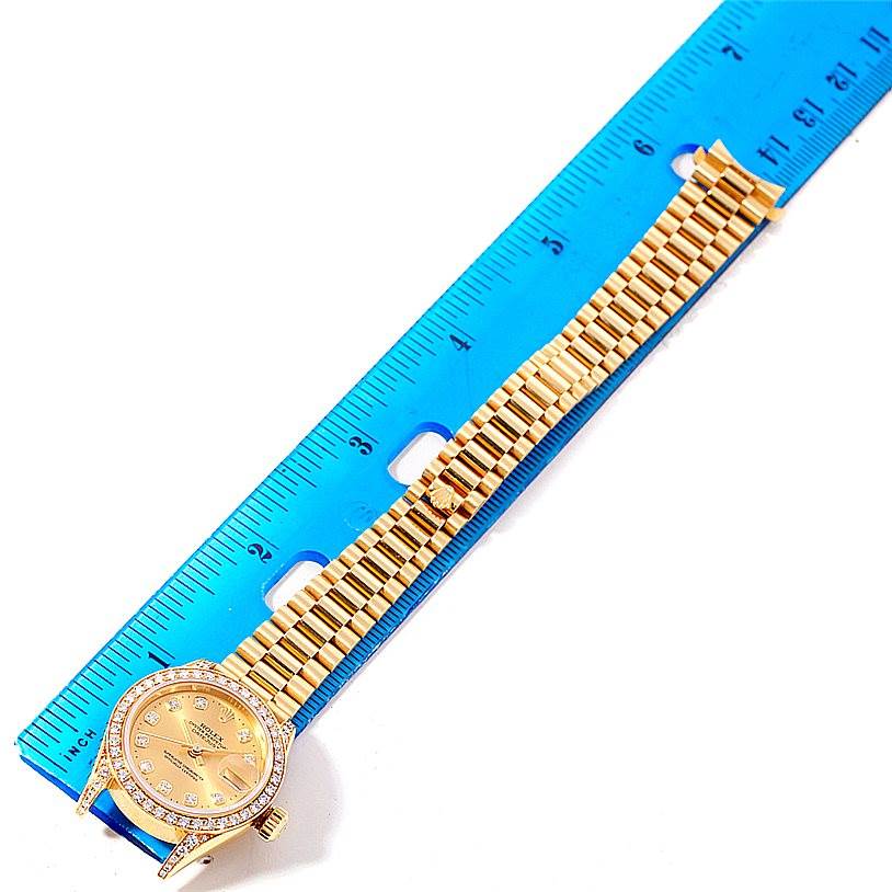 The Rolex President 69158 Women's Yellow Gold Champagne Dial 69158 Women's Yellow Gold Champagne Dial model watch is shown from an overhead angle, highlighting the dial, bezel, and part of the bracelet against a blue ruler.