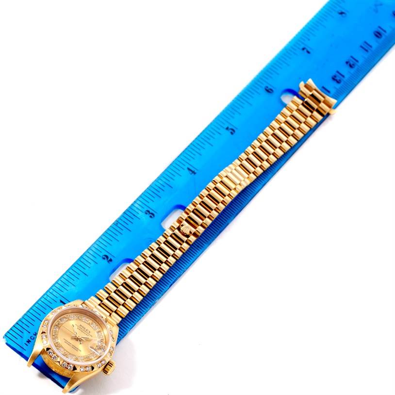 The Rolex President 69178 Women's Yellow Gold Champagne Dial 69178 Women's Yellow Gold Champagne Dial model watch is shown from a top-down angle, displaying its face, bezel, and full bracelet alongside a ruler.