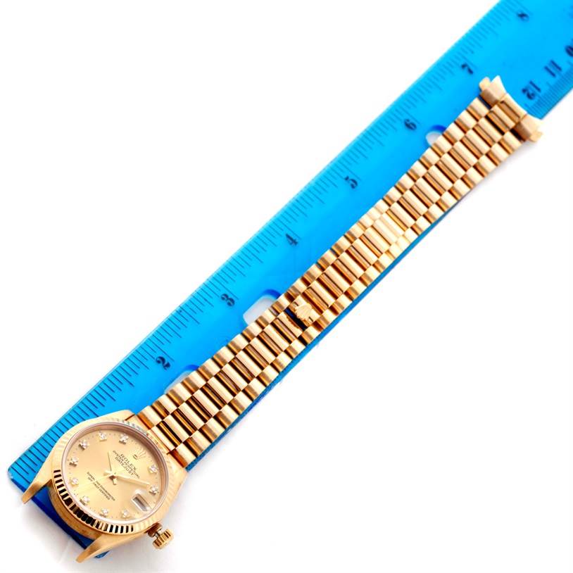 The image shows a Rolex President 68278 Women's Yellow Gold Champagne Dial 68278 Women's Yellow Gold Champagne Dial model watch laid flat beside a blue ruler, highlighting its band and face.