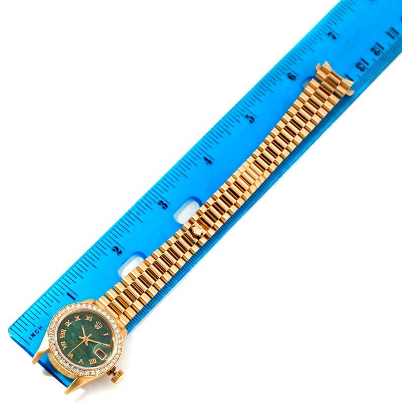 The image shows a Rolex President 69178 Women's Yellow Gold Green Dial 69178 Women's Yellow Gold Green Dial model watch positioned next to a blue ruler, featuring the face and full band.