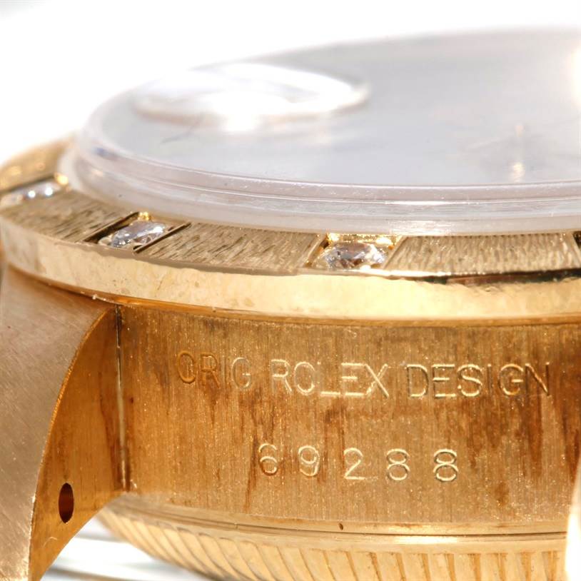The image shows a close-up of the side and part of the bezel of a Rolex President 69288 Women's Yellow Gold White Dial 69288 Women's Yellow Gold White Dial model watch, revealing its serial number and diamond-encrusted details.