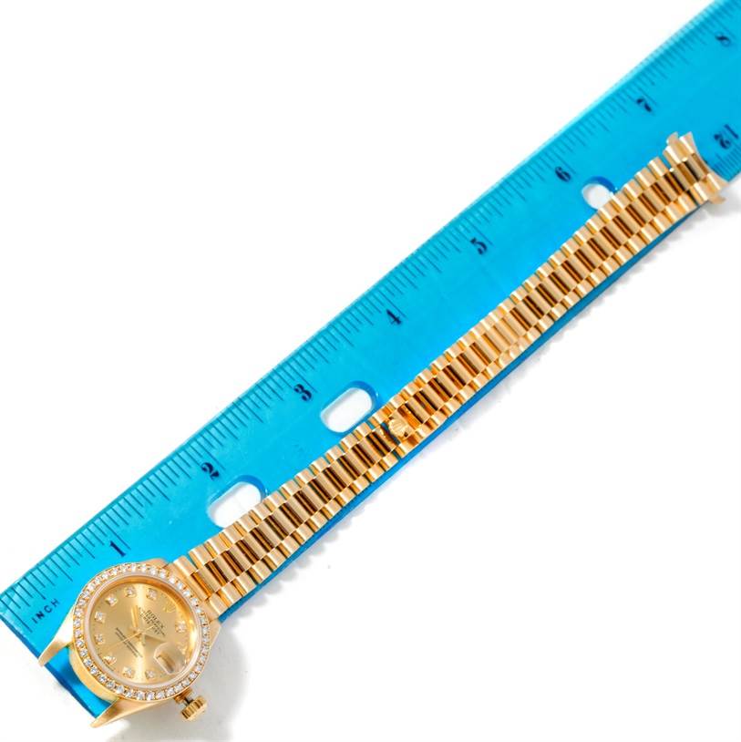 This image shows the face and bracelet of a Rolex President 69178 Women's Yellow Gold Champagne Dial 69178 Women's Yellow Gold Champagne Dial model watch placed next to a blue ruler for measurement.