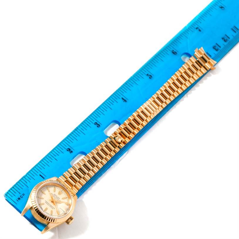 The Rolex President 69178 Women
s Yellow Gold Beige Dial 69178 Women
s Yellow Gold Beige Dial model watch is shown from an overhead angle, featuring its face and bracelet placed next to a ruler.