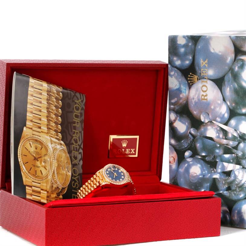 The image shows a Rolex President 69188 Women's Yellow Gold Blue Dial 69188 Women's Yellow Gold Blue Dial model watch with the watch and manual inside an open red box with a patterned outer box beside it.