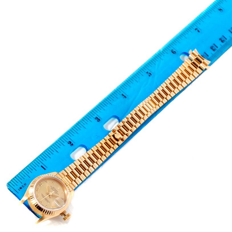 The image shows a Rolex President 69178 Women's Yellow Gold Champagne Dial 69178 Women's Yellow Gold Champagne Dial model watch laid flat beside a blue ruler, displaying its band and face.