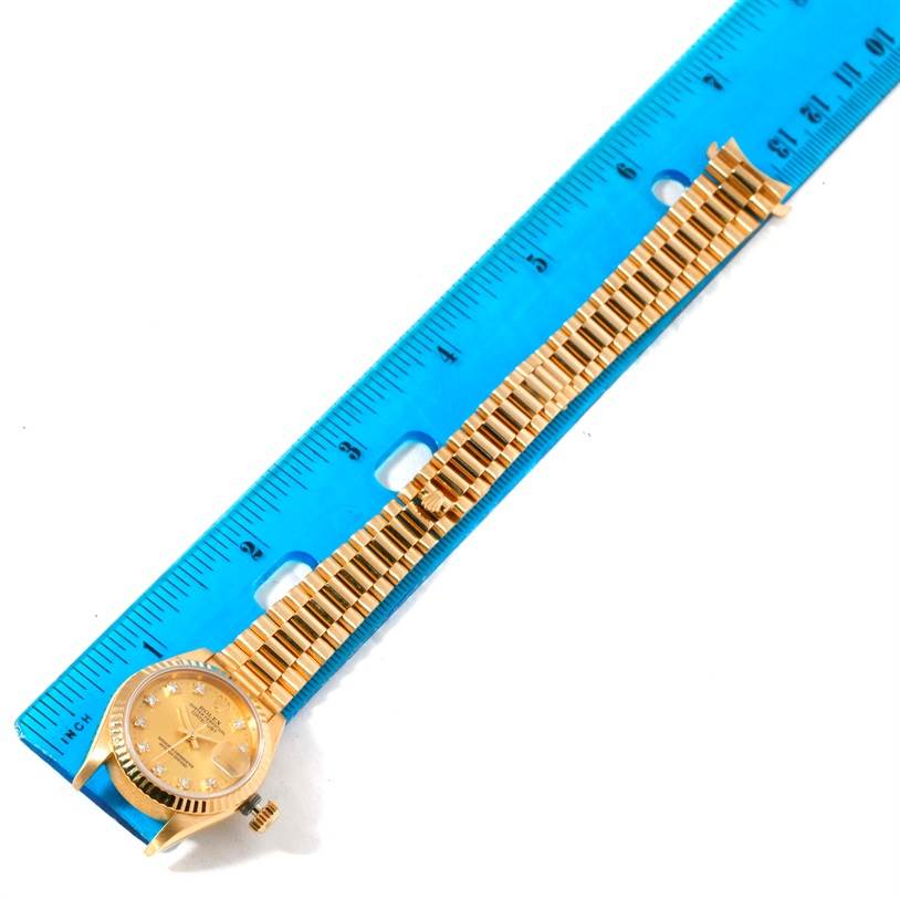 A Rolex President 69178 Women's Yellow Gold Champagne Dial 69178 Women's Yellow Gold Champagne Dial watch is shown at a top-down angle, with its gold band measured against a blue ruler.